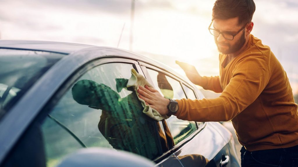 Homem limpando áreas do carro com uma caseira solução para limpar os vidros.