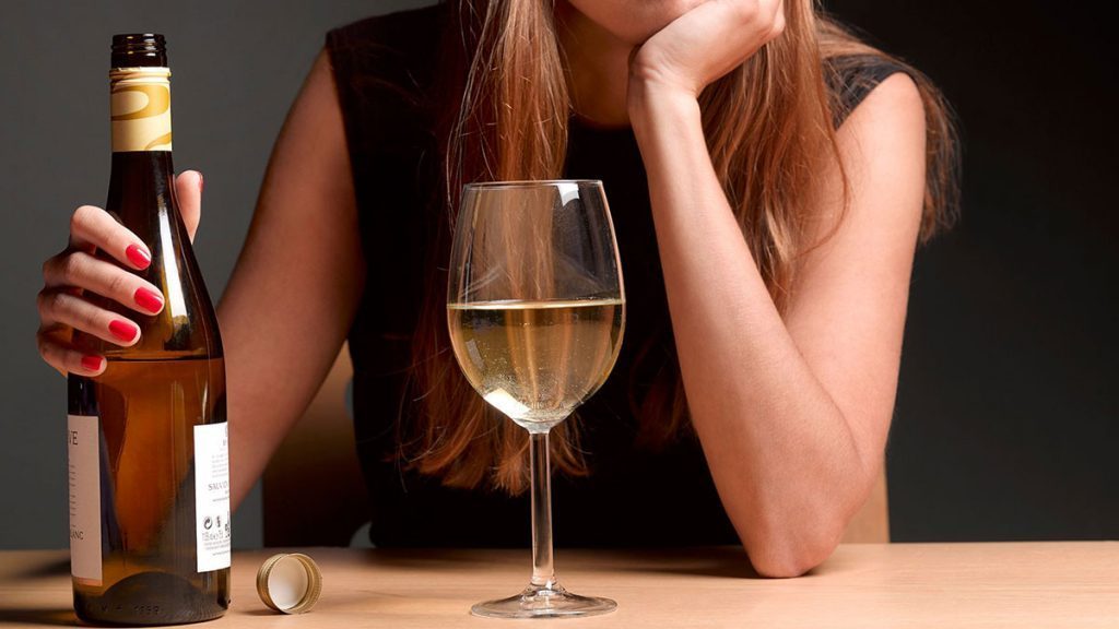 Mulher bebendo taça de bebida alcoólica e apresentando sinais de ansiedade. Álcool é um dos alimentos que causam a ansiedade.